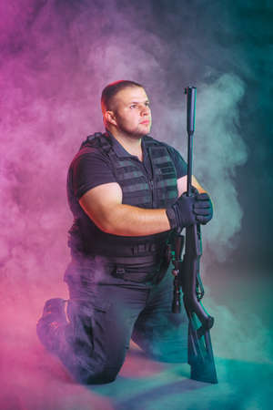 Soldier comes out of the smoke on the battlefield. The concept of military special operations. Kneeling and posing with shotgunの写真素材