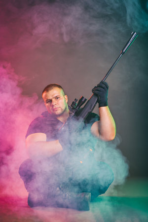 Soldier comes out of the smoke on the battlefield. The concept of military special operations. Sitting and posing with shotgunの写真素材