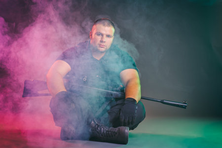 Soldier comes out of the smoke on the battlefield. The concept of military special operations. Sitting and posing with shotgunの写真素材