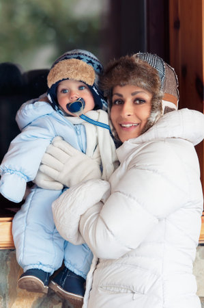 Happy mother holding her baby son sitting outdoor on the window. Winter season.の写真素材