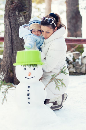 Happy mother and her baby boy playing with snowman on winter day. Christmas timeの写真素材