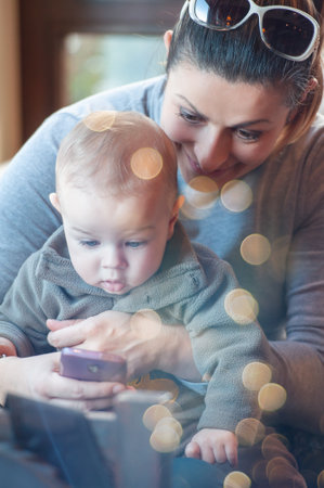 Happy mother holding her baby son in the lap and showing some content on the cell phone. Winter seasonの写真素材