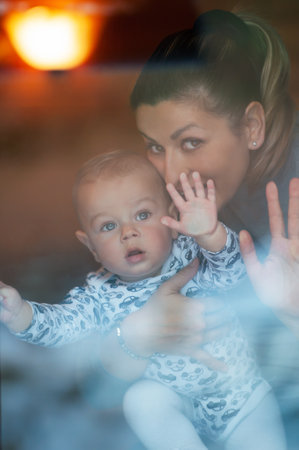 Happy mother and her baby boy looking throw the window and playing in warm home on winter day. Christmas time.の写真素材