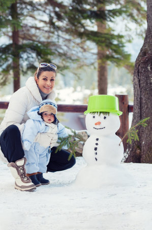 Happy mother and her baby boy playing with snowman on winter day. Christmas timeの写真素材
