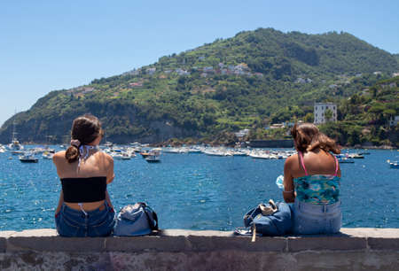 girls on a low wall with the sea in the background in Ischiaの写真素材