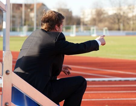 Spectator trainer or coach sitting in stadium next to the running track pointing with his handの写真素材