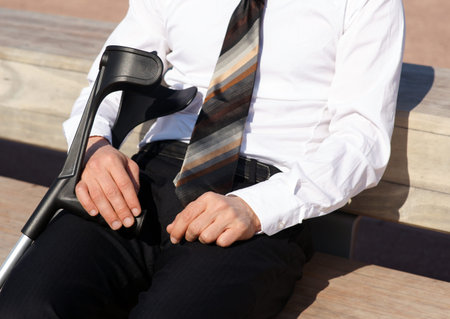 Businessman sits in a park in the city with crutches after knee injury