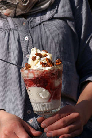 Young woman holds delicious ice cream sundae bowl glas vanilla strawberry walnutの写真素材