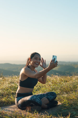 A cheerful young woman in sports clothing having video chat outdoors, smiling and wavingの写真素材