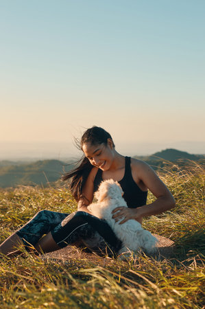 A happy young woman sitting on the grass playing with her beautiful puppy dogの写真素材