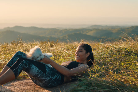 A woman laying on the grass and playing with her puppy dog after exercising