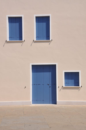 Closed blue windows and door on wall of mediterranean house during the siesta timeの写真素材