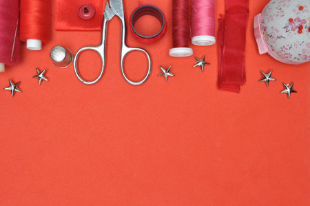 Sewing kit tool, scissors, thread and accessories on a red background