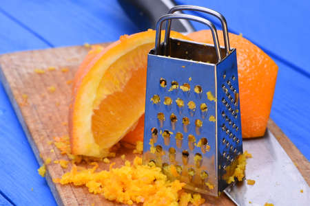 Orange fruit and orange zest with grater on wooden boardの写真素材