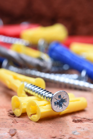 Screws plasctic dowels and tool on brick background close-up