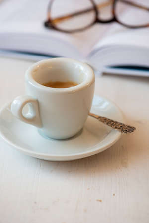 Cup of coffee espresso and book with reading glasses in backgroundの写真素材