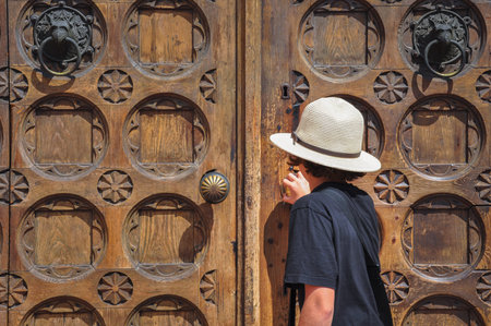 Boy with summer hat opens big old front door and seeks shelter from the heatの写真素材