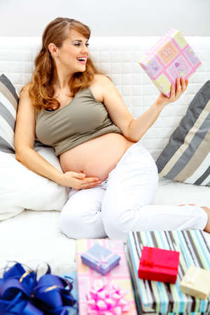 Happy  beautiful pregnant woman sitting on sofa at home with gifts for her unborn baby
の写真素材