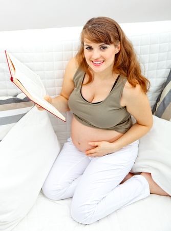 Smiling beautiful pregnant woman sitting on sofa at home with book.
の写真素材