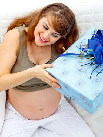 Smiling  beautiful pregnant woman sitting on couch with gift for her unborn baby
の写真素材
