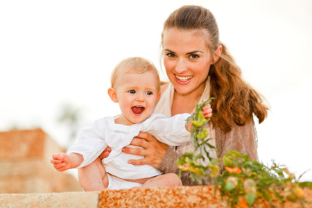 Portrait of happy mother and laughing baby playing with plants 
