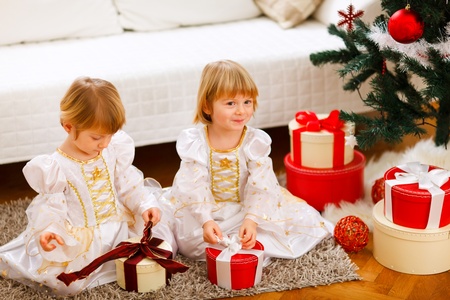 Two cute twins girls opening presents near Christmas treeの写真素材