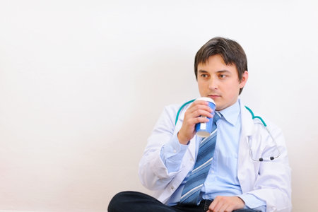 Tired medical doctor sitting on floor with coffeeの写真素材