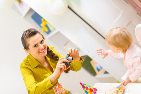 Happy mother making photos of celebrating first birthday baby