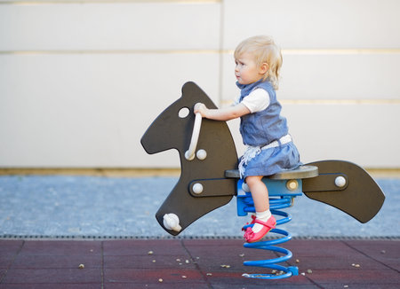 Happy baby swinging on horse on playground. Side viewの写真素材