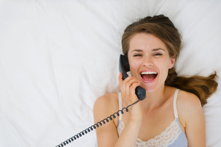 Portrait of woman laying on bed and speaking phone. Upper view