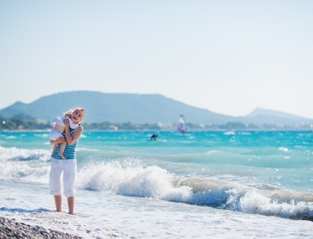 Baby hugging mother standing at sea shoreの写真素材