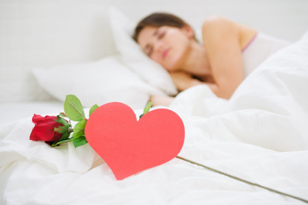 Closeup on red rose and heart shaped postcard near sleeping womanの写真素材