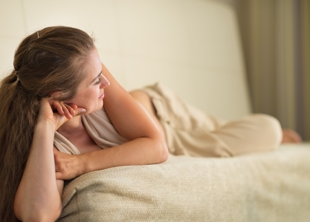 Thoughtful young woman laying on couch and looking on copy spaceの写真素材