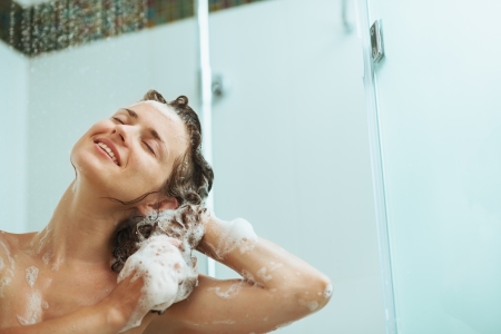 Happy woman washing hair with shampoo under water jetの写真素材
