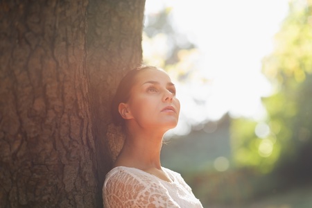 Thoughtful young woman lean against treeの写真素材