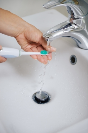 Closeup on hands washing electric toothbrush under water streamの写真素材
