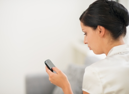 Young woman sitting on sofa and reading sms on mobile phone. Rear viewの写真素材