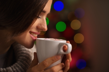 Happy young woman enjoying cup of hot beverage in front of Christmas lightsの写真素材