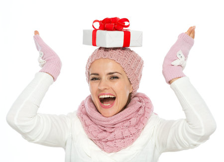 Happy woman in knit winter clothing balancing Christmas present box on head