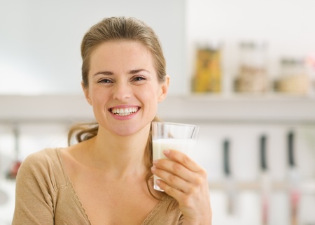 Portrait of smiling young woman with glass of milk in kitchenの写真素材