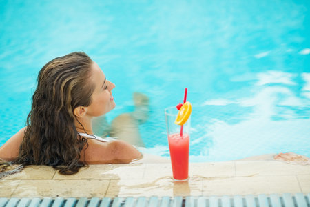 Young woman at pool with cocktail. rear viewの写真素材