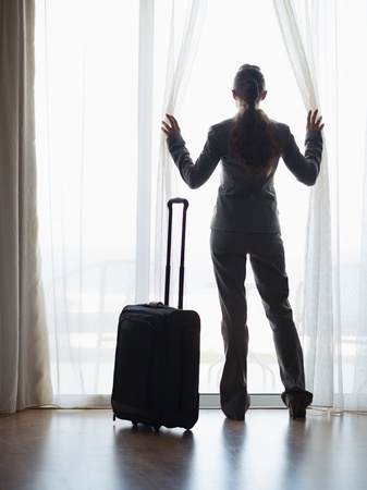 Silhouette of business woman with wheel bag looking into hotel window . rear viewの写真素材
