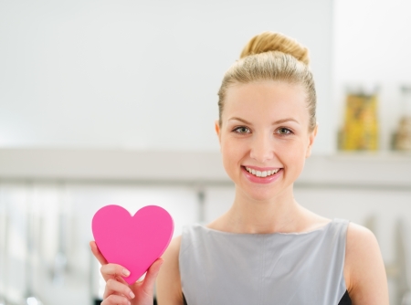 Happy young housewife showing decorative heart in kitchenの写真素材