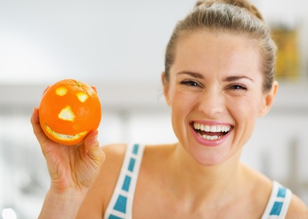 Smiling young woman showing orange with funny faceの写真素材