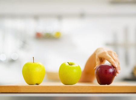 Closeup on hand choosing between two green and one red apple on cutting board