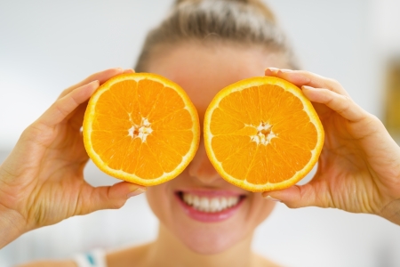 Happy young woman holding two slices of orange in front of eyesの写真素材