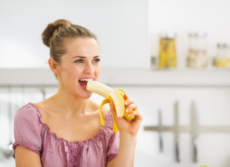 Young woman eating banana in kitchenの写真素材