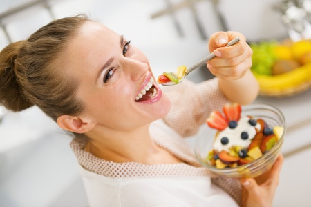 Happy young housewife eating fruits salad . rear view