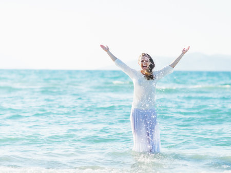 Smiling young woman standing in sea and sprinkling waterの写真素材