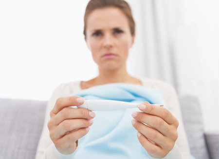 Closeup on thermometer in hand of concerned young woman